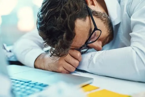 Overworked man lying on laptop